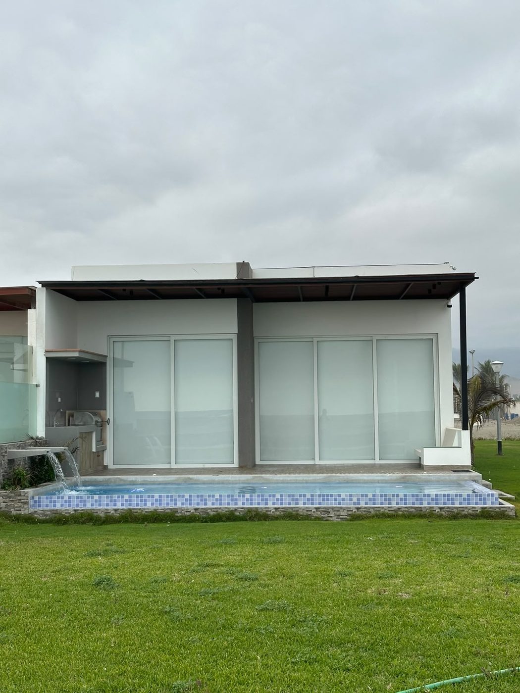 Casa de playa con piscina revestida en venecitas y caídas de agua, vista desde el jardín