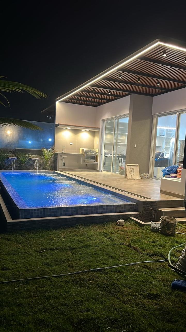 Piscina iluminada de noche con terraza y pérgola